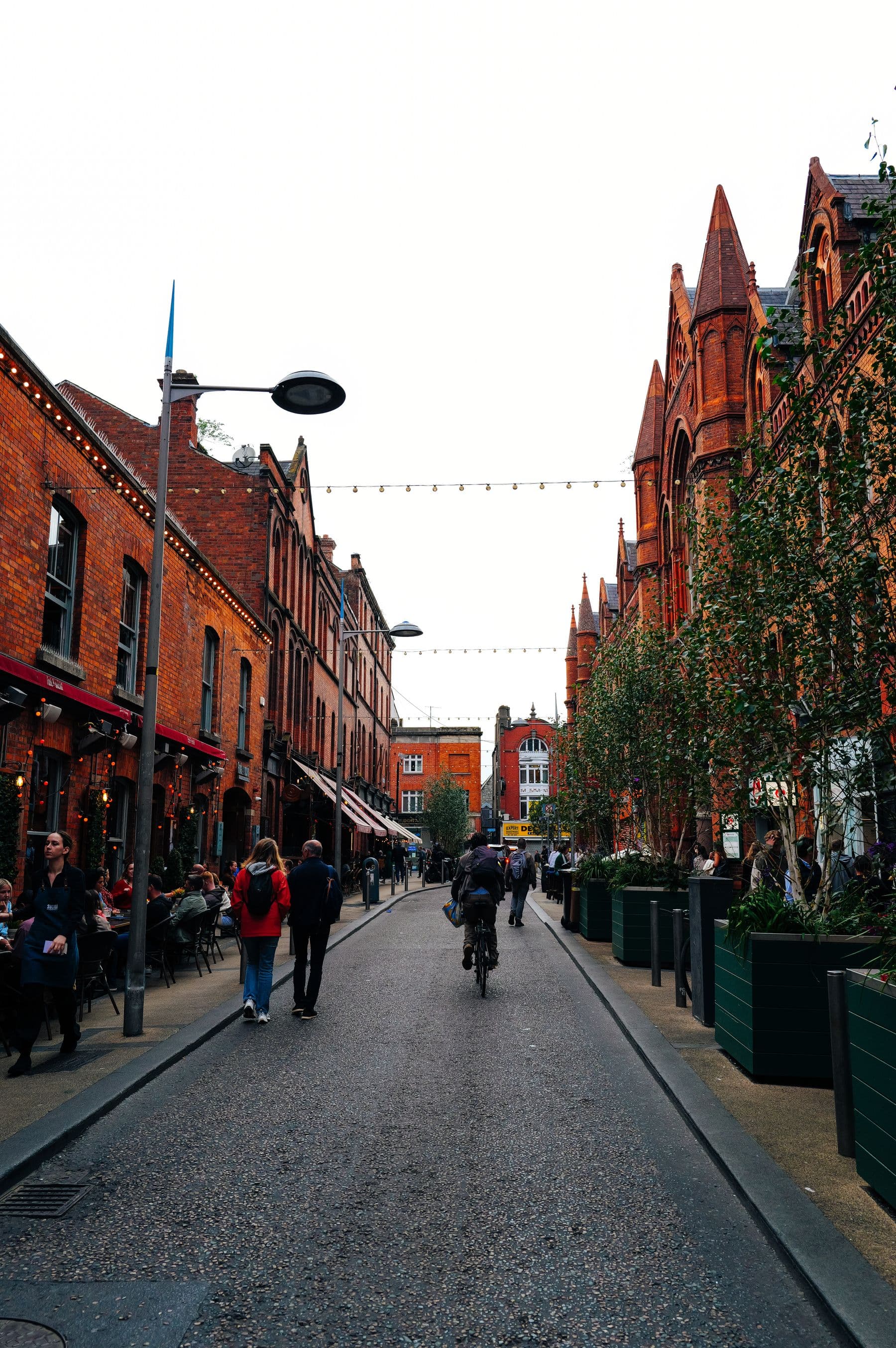 People walking and cycling along a brick-lined neighborhood commercial street.